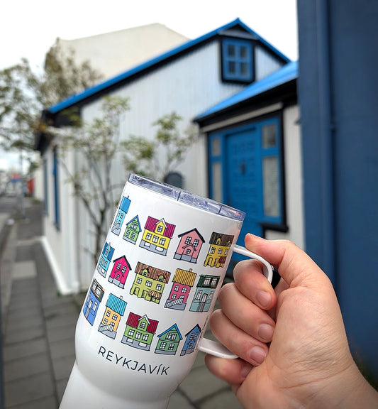 Hand holding a travel mug with colorful houses of 'Reykjavik', with Reykjavik building in the background