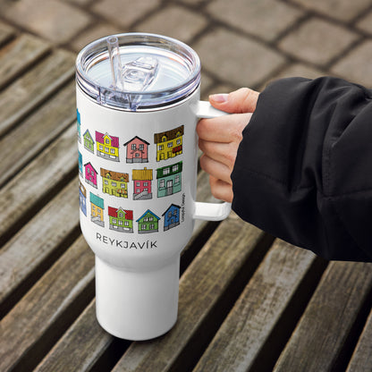 White travel mug with colorful house design and 'Reykjavök' text, held by a person on a wooden surface.